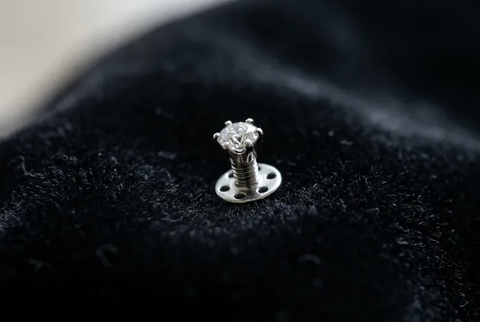 Causes et signes d'un rejet de piercing microdermal Bijou de piercing microdermal posé sur un fond sombre, vue minimaliste