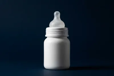 Vue rapprochée et minimaliste d'un biberon sur fond bleu marine.